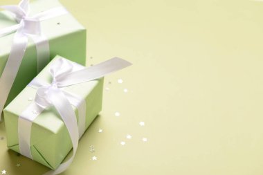 Beyaz kurdeleli hediye kutuları ve zeytin arka planında konfeti.