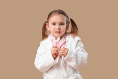 Kahverengi arka planda diş fırçası olan bornozlu tatlı küçük bir kız.