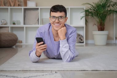 Evde cep telefonu olan şık gözlüklü yakışıklı bir genç.