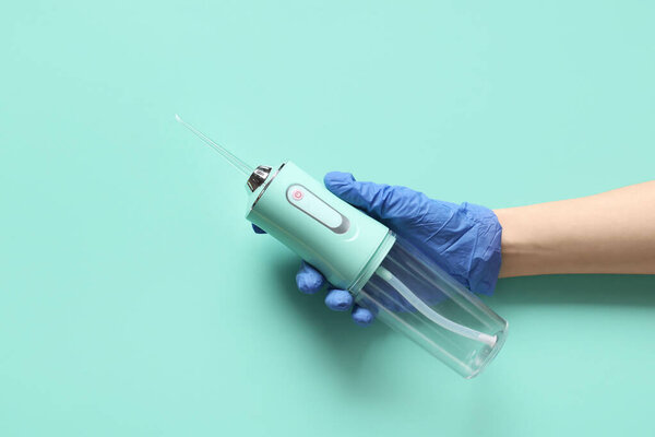 Dentist's hand in medical glove holding oral irrigator on color background