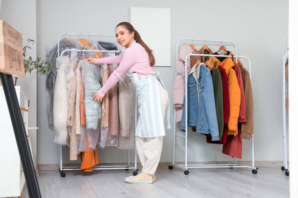 Молодая работница возле вешалок для одежды в химчистке