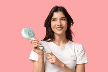 Pembe arka planda mavi saç fırçası olan güzel bir genç kadın.