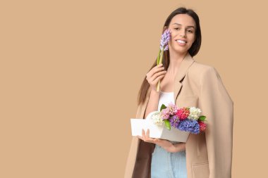 Mutlu gülümseyen genç kadın elinde sepetle bej arka planda sümbül çiçekleri tutuyor.