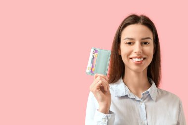 Pembe arka planda kredi kartı sahibi gülümseyen genç bir kadın.