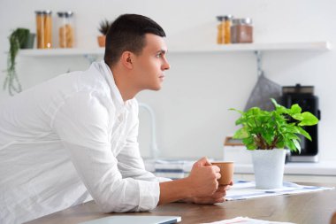 Modern mutfakta masaya yaslanmış bir fincan kahveyle yakışıklı genç bir adam.