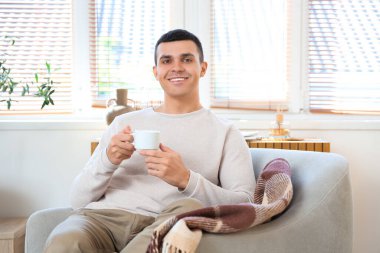 Modern oturma odasındaki koltukta oturan bir fincan kahveli yakışıklı genç adam.