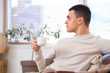 Modern oturma odasındaki koltukta oturan bir fincan kahveli yakışıklı genç adam.