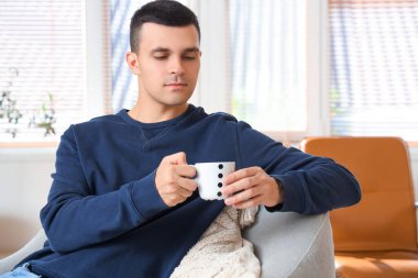 Modern oturma odasındaki koltukta oturan bir fincan kahveli yakışıklı genç adam.