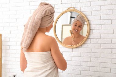 Güzel, genç bir kadın, masaj fırçasıyla banyoda aynaya bakıyor.