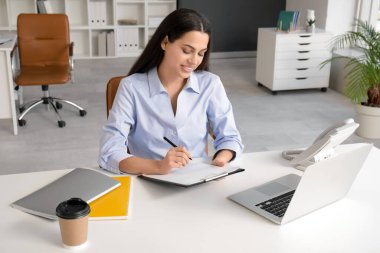 Güzel iş kadını ışık ofisindeki panoya yazı yazıyor.