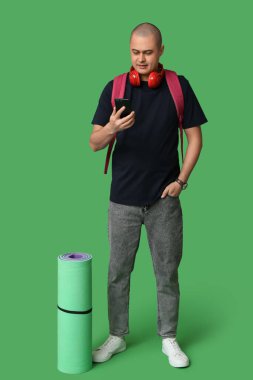 Kulaklıklı genç erkek turist, yeşil arka planda seyahat minderi ve cep telefonu var.