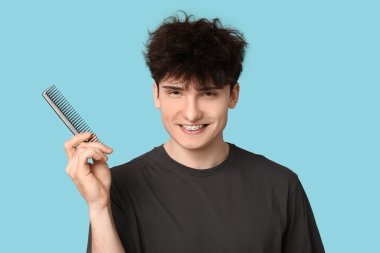 Mavi arka planda tarağı olan koyu renk saçlı genç adam.