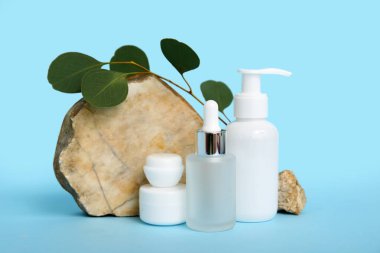 Şişelerle, kozmetik ürünlerle dolu kavanozlarla, mavi arkaplanda taş ve dallarla kompozisyon