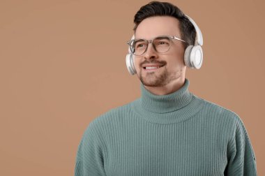 Kahverengi arka planda gözlüklü ve kulaklıklı yakışıklı bir genç.