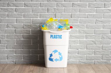 Gri tuğla duvarın yanında PLASTIC işareti olan tam çöp kutusu. Geri dönüşüm kavramı