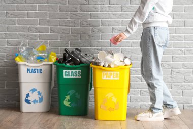 Gri tuğla duvarın yanındaki çöplerin olduğu çöp kutularına çöp atan bir kadın. Geri dönüşüm kavramı