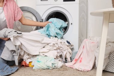 Kirli çamaşırları evdeki çamaşır makinesine koyan genç bir kadın.