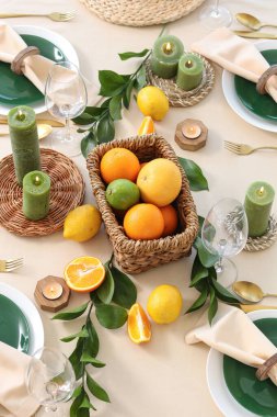 Narenciye meyveleri, yanan mumlar ve açık masa örtüsünün üzerindeki yeşil yapraklarla dolu güzel bir masa.