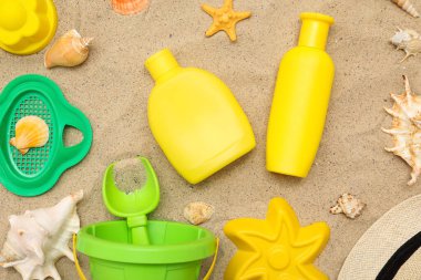 Kum üzerindeki çocuklar için güneş kremi ve plaj aksesuarlarıyla harika bir kompozisyon.