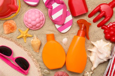 Kum arka plandaki çocuklar için güneş kremi ve plaj aksesuarlarıyla güzel bir kompozisyon