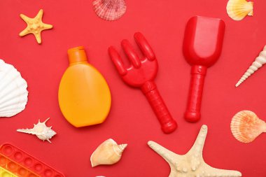 Kırmızı arka plandaki çocuklar için güneş kremi ve plaj aksesuarlarıyla güzel bir kompozisyon