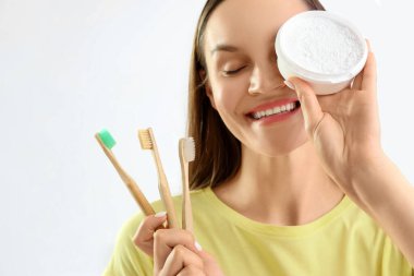 Hafif arka planda diş pudrası ve bambu fırçalarıyla gülümseyen genç kadın, yakın plan.