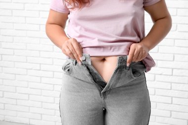 Dar kotlu, beyaz tuğlalı arka planda şişman bir kadın. Aşırı ağırlık kavramı