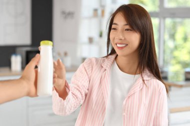 Pijamalı güzel bir Asyalı kadın evde başka birinden şişe lezzetli yoğurt alıyor.