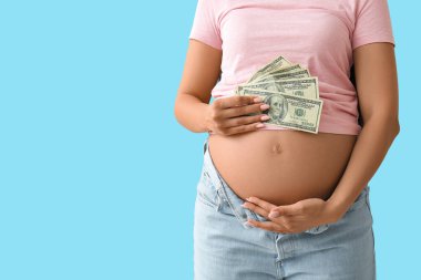 Mavi arka planda dolar banknotları olan hamile bir kadın, yakın plan. Annelik Faydası konsepti