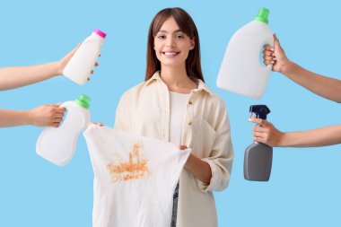 Lekeli elbiseleri ve mavi arka planda çamaşır deterjanı olan genç bir kadın.