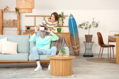 Genç bir kadın ve erkek arkadaşı evde VR gözlüğü kullanıyorlar.