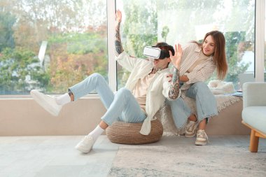 Genç bir kadın ve erkek arkadaşı evde VR gözlüğü kullanıyorlar.