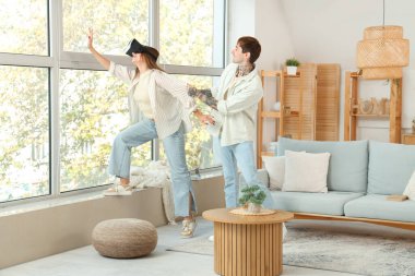 Genç adam ve kız arkadaşı evde VR gözlüğü kullanıyorlar.