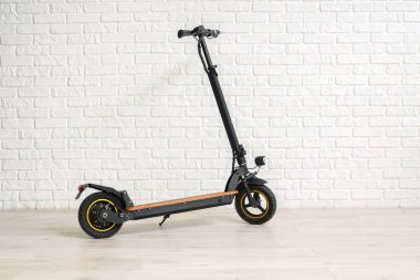 Modern elektrikli scooter beyaz tuğla duvarın yanında.