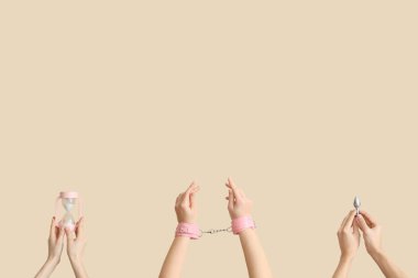 Female hands with hourglass, handcuffs and butt plug on beige background
