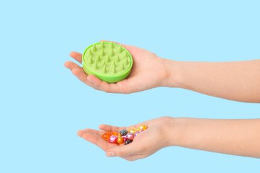 Silikon kafa masajı fırçası ve mavi arka planda saç vitamini kapsülleri olan kadın eli.