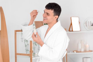 Banyoda yüzüne serum süren genç bir adam.
