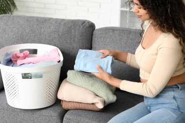 Çamaşır sepetiyle evde temiz giysileri katlayan güzel, mutlu, Afro-Amerikalı bir kadın.