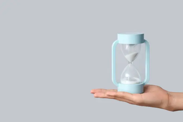 stock image Female hand holding hourglass on grey background