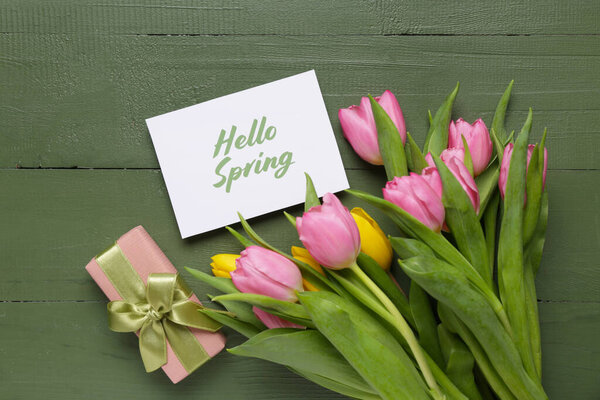 Greeting card with text HELLO SPRING, gift box and beautiful tulips on green wooden background