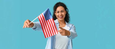 Güzel, mutlu Afro-Amerikalı kadın, açık mavi arka plandaki izleyiciyi işaret eden ABD bayrağıyla.