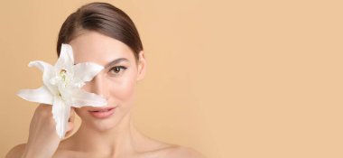 Bej arka planda zambak çiçeği olan güzel genç bir kadın.