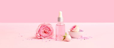 Pembe arka planda bir şişe gül yağı ve deniz tuzu.
