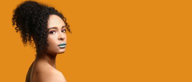 Turuncu arka planda olağandışı makyajı olan güzel Afro-Amerikan kadın portresi.