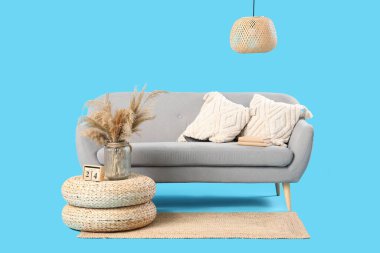 Modern oturma odası içi gri kanepe, hasır puflar ve mavi arka planda saman lamba.