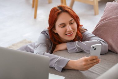 Evde cep telefonu kullanan pijamalı genç bir kadın.