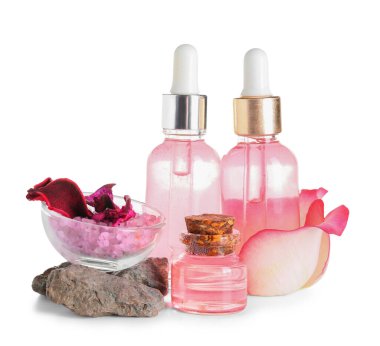 Beyaz zemin üzerinde gül özü ve taşlar olan kozmetik yağı şişeleri.