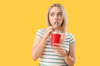 Sarı arka planda bir bardak gazozu olan genç ve düşünceli bir kadın.