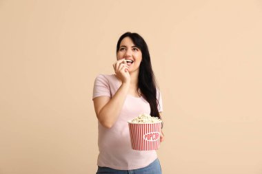 Bej arka planda bir kova patlamış mısırı olan mutlu genç bir kadın.