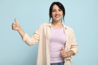 Mavi arka planda baş parmağını gösteren mutlu genç esmer portresi